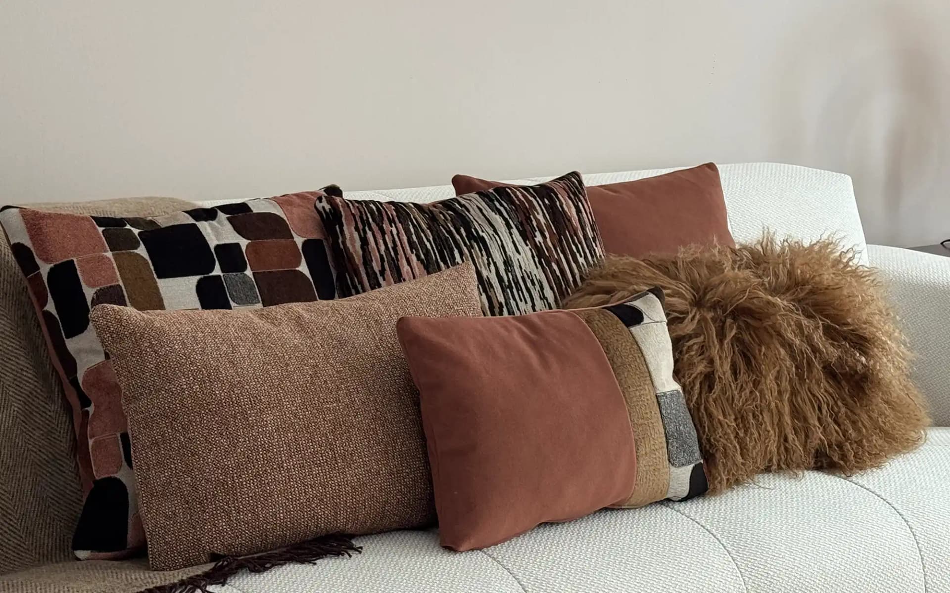 Sfeerfoto met verschillende formaten kussens in terra kleuren gecombineerd met een plaid en een schapenvacht kussen