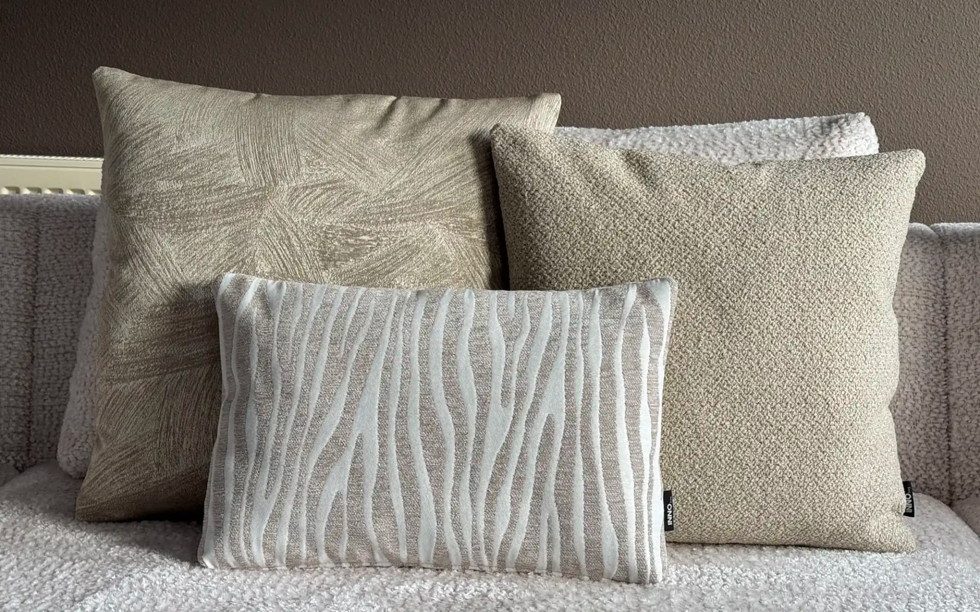Sierkussen set Be Rhythm beige met drie stijlvolle sierkussens op een lichte bank